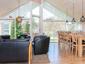 A spacious living area with a large sofa, a dining table with chairs, and a view through large windows.