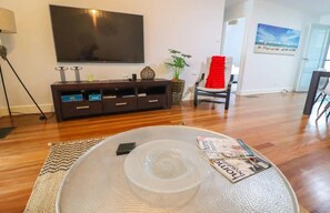 A living room with a large flat-screen TV mounted on the wall, a dark wooden entertainment unit, a red chair, a potted plant, and a magazine on a round table.