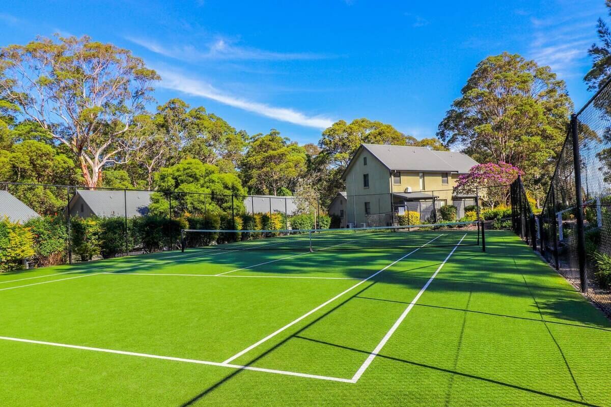 A tennis court with a net, surrounded by trees and a house in the background.