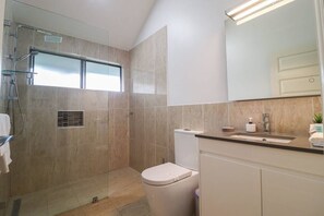 A modern bathroom with a glass-enclosed shower, a toilet, and a sink with a mirror above. - Blue Lago at Raffertys Resort (Cams Wharf)