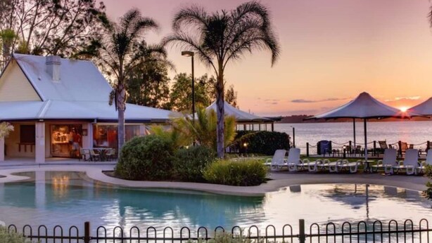 A resort pool area with a sunset view, lounge chairs, and a building with a bar. - Blue Lago at Raffertys Resort (Cams Wharf)