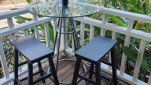 A glass-top table with two black chairs on a wooden deck, surrounded by white railings and lush greenery. - Blue Lago at Raffertys Resort (Cams Wharf)