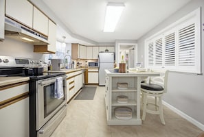 Una cocina moderna con electrodomésticos integrados, un comedor con mesa y sillas blancas, y una ventana con persianas.