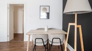 Et spiseområde med et bord, stole, en lampe og et billede i ramme på væggen.