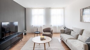 En moderne stue med et fladskærms-tv, et rundt sofabord, en sofa og to lænestole.