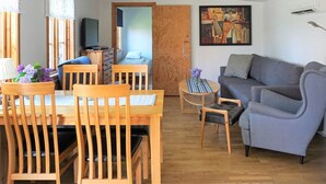 Una sala de estar con un sofá, una mesa de comedor con sillas, un televisor y un cuadro en la pared.