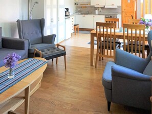 A living room with a sofa, armchair, ottoman, and a dining table with chairs.