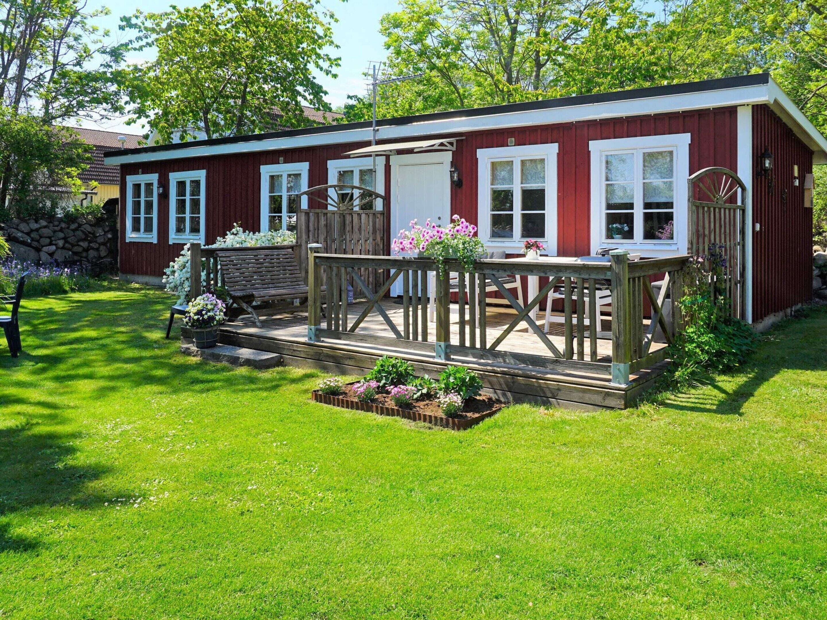 A red wooden building with white trim, a porch with a wooden railing, and a garden with flowers and a bench.