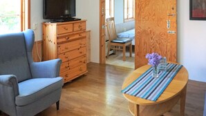 Una sala de estar con un sillón azul, un aparador de madera, un televisor y una mesa de comedor con mantel a rayas.