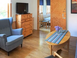 Uma sala de estar com uma poltrona azul, um aparador de madeira, uma televisão e uma mesa de jantar com um jogo americano listrado.
