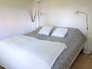 A neatly made bed with a white duvet and two pillows, a floor lamp, and a vase with branches on a bedside table. - 5 Person Holiday Home in Solvesborg (Sölvesborg)