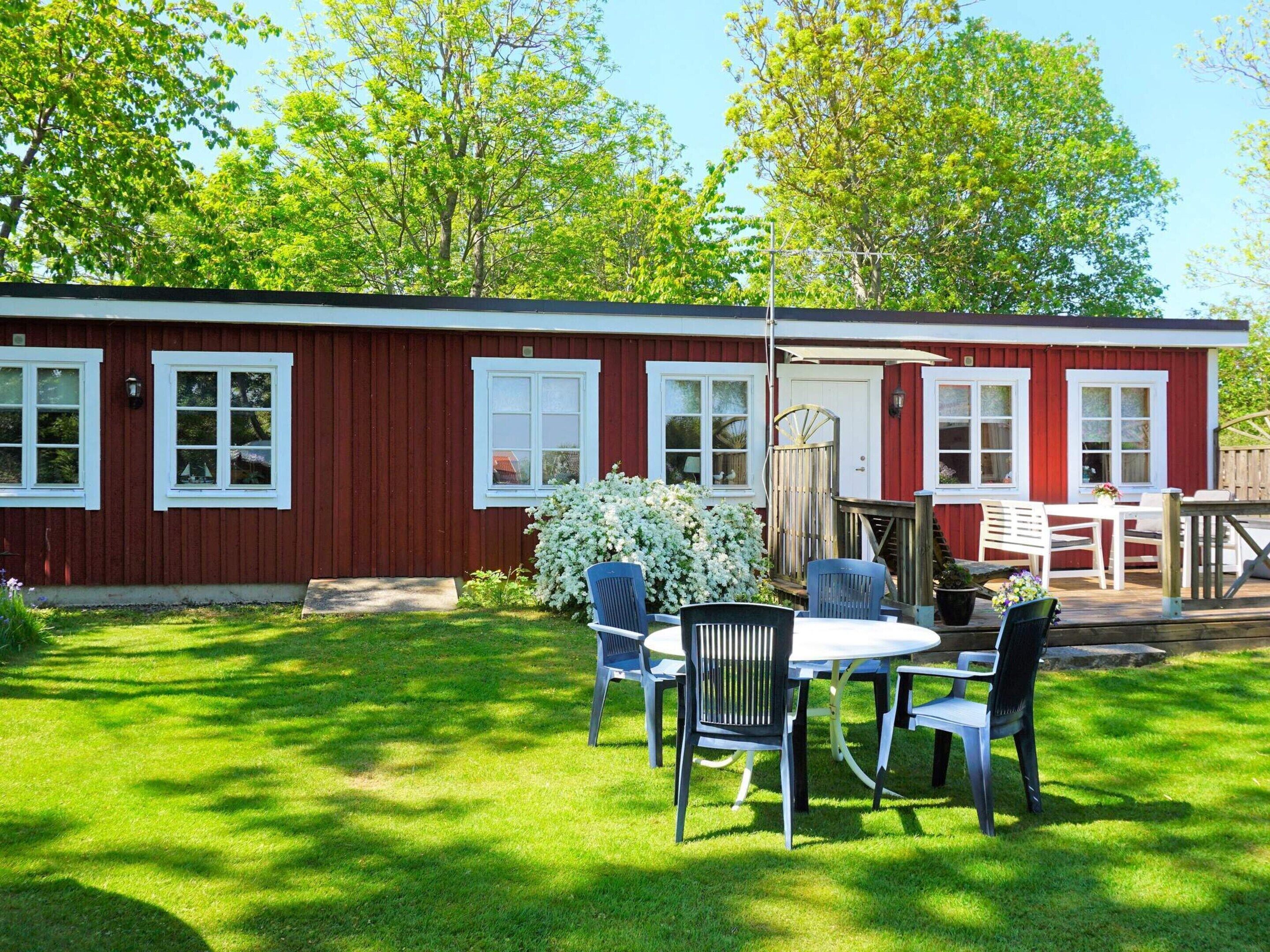 A red building with white trim, a covered patio with a table and chairs, and a well-maintained lawn.