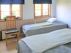 A room with two beds, a chair, and a window with a view of greenery.