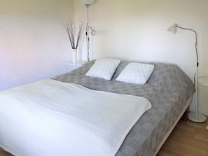 A neatly made bed with a white duvet and two pillows, a floor lamp, and a vase with branches on a bedside table. - 5 Person Holiday Home in Solvesborg (Sölvesborg)