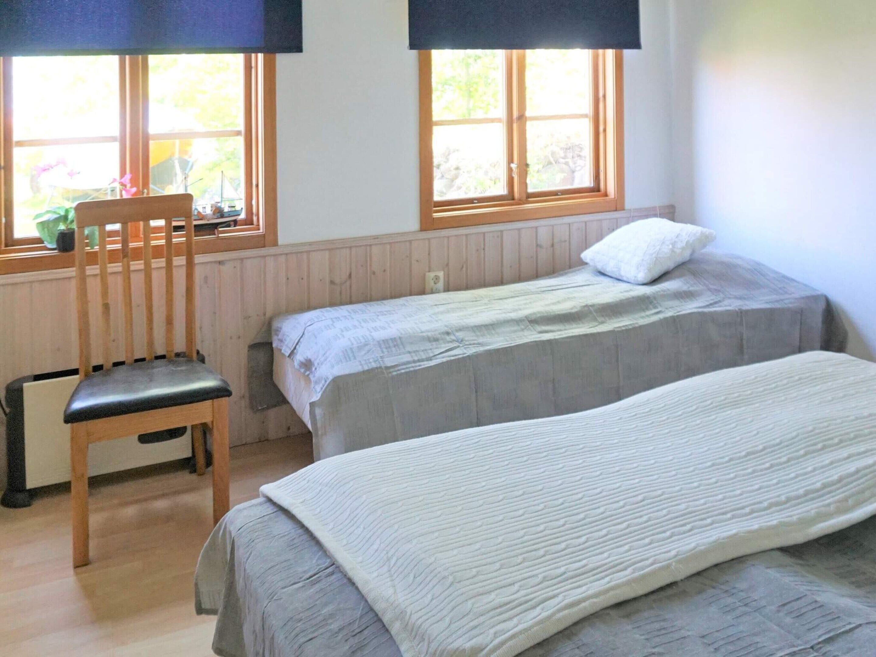 Quarto com duas camas, uma cadeira e janela com vista para o verde.