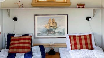 Un dormitorio con dos camas, un cuadro enmarco de un barco y una mesita de noche con una lámpara.