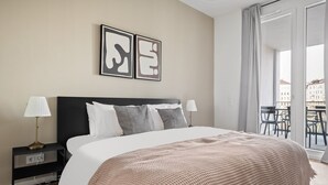 Une chambre d’hôtel moderne avec un grand lit, deux lampes de chevet, une table de nuit noire et une vue sur la ville depuis un balcon.