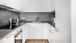 Une cuisine moderne avec des meubles blancs, un plan de travail noir, un évier en acier inoxydable et un four à micro-ondes.