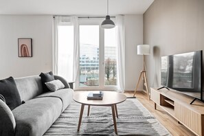 A modern living room with a grey sofa, a round coffee table, a TV on a wooden stand, and a floor lamp.