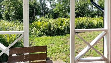 A wooden bench in a covered outdoor area with a view of a garden and trees.