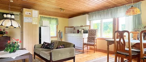 En ombonad inredning med ett träpanelat tak, en soffa, ett matbord med stolar och ett köksområde.