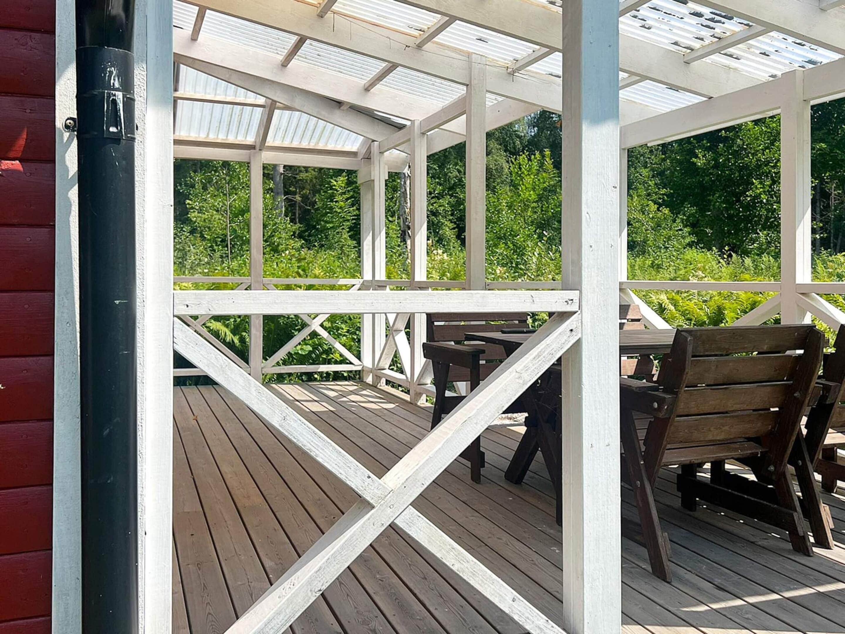 Una terraza de madera cubierta con mesas y sillas, rodeada de follaje.