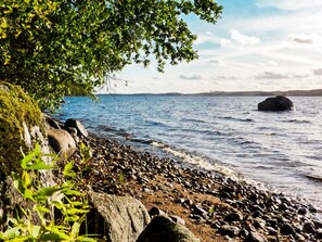 A rocky shoreline with calm water, a tree, and distant land. - 4 Person Holiday Home in Braas (Braås)