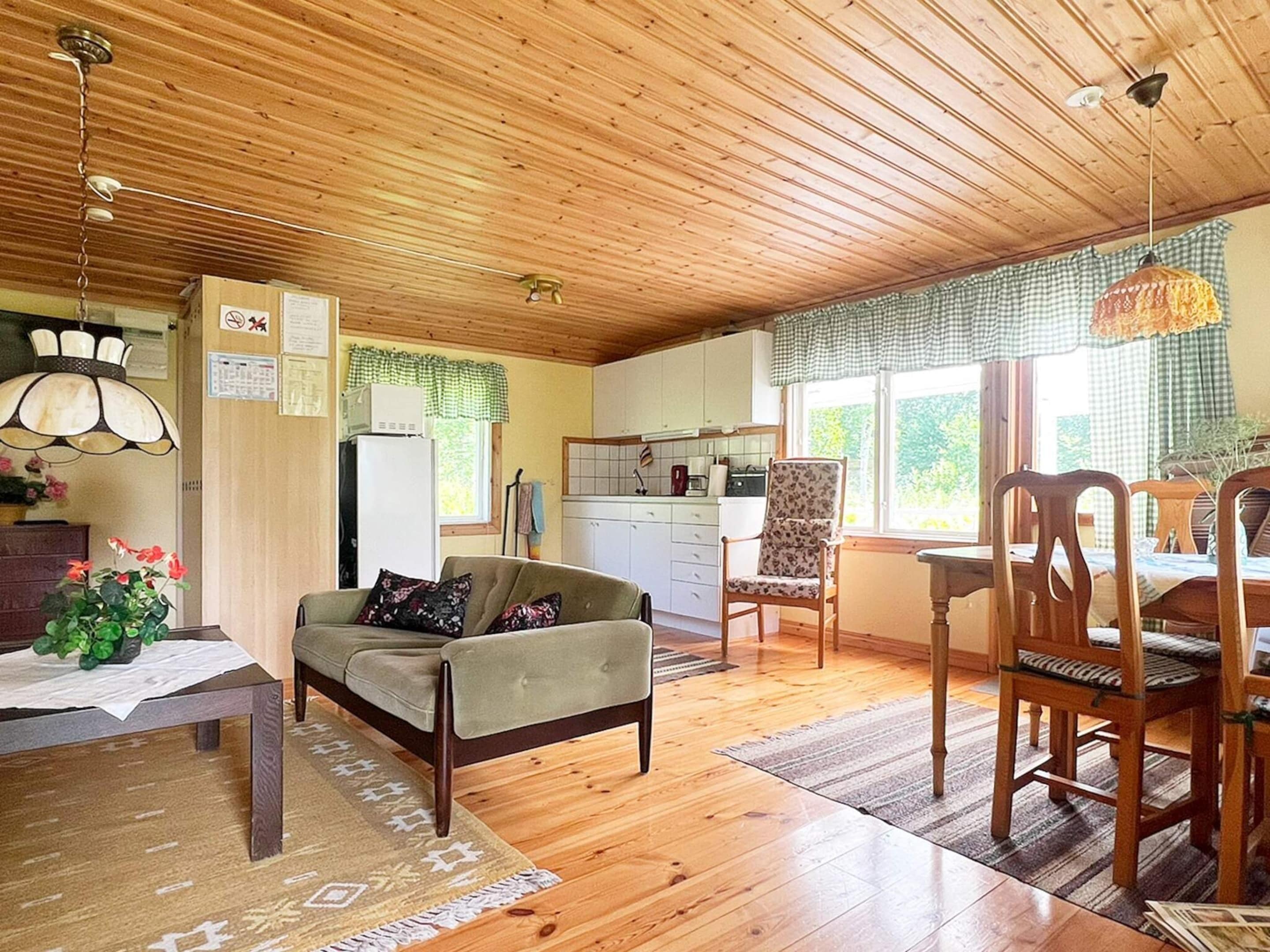 Una sala de estar acogedora con un sofá, una mesa de comedor y sillas, una cocina con armarios y un refrigerador, y un ventilador de techo.