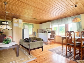 Ein gemütliches Wohnzimmer mit einer Couch, einem Esstisch und Stühlen, eine Küchenzeile mit Schränken und einem Kühlschrank sowie ein Deckenventilator.