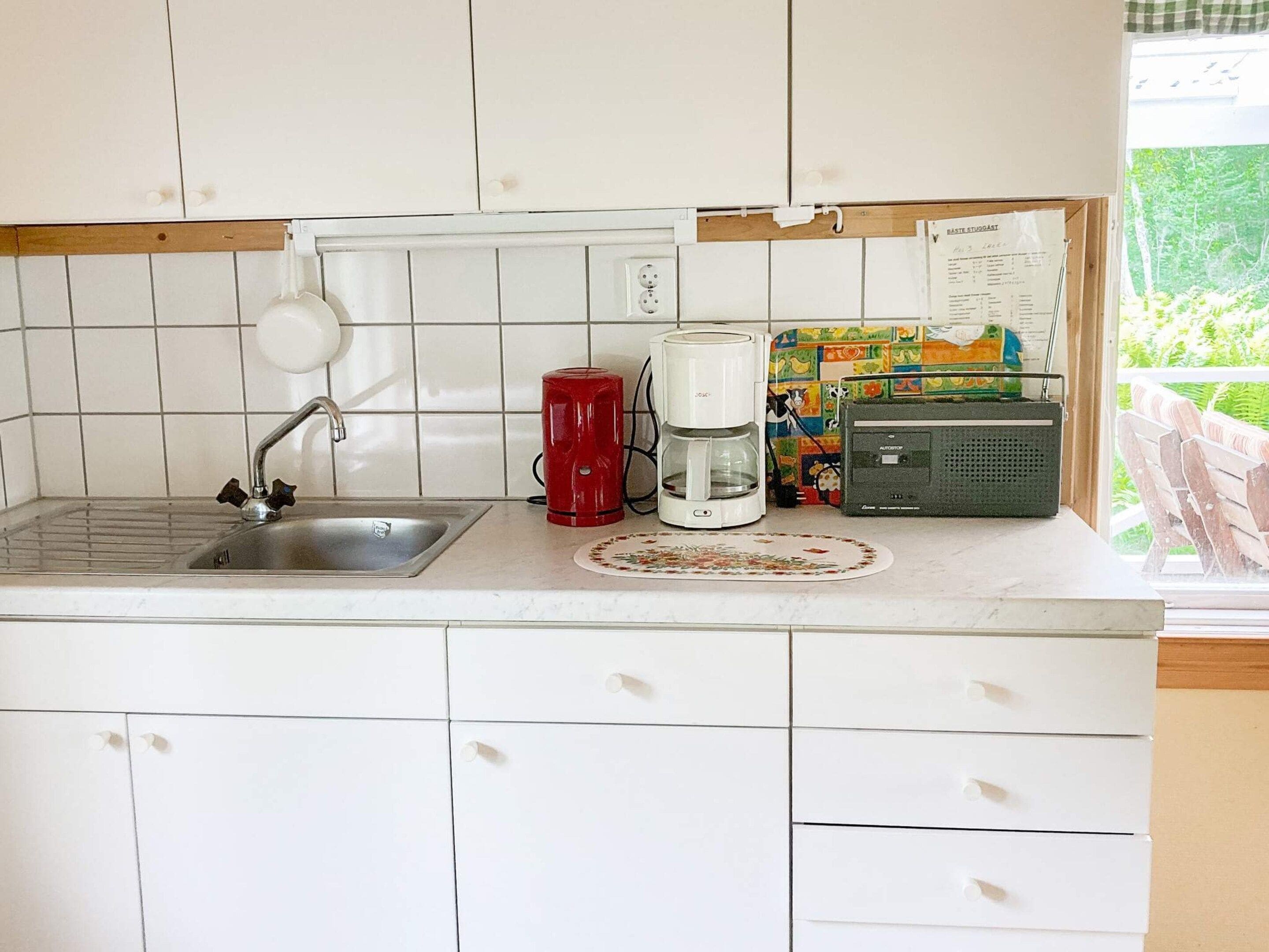 A kitchen with a sink, a red coffee maker, a white coffee maker, and a radio.