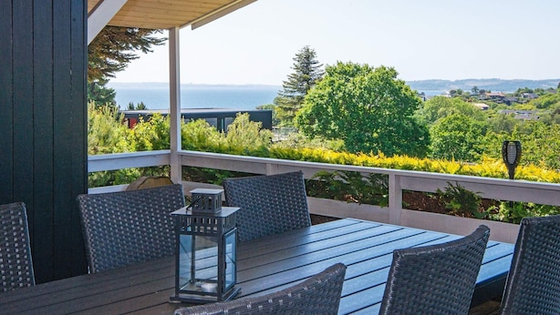 A covered outdoor seating area with a table and chairs, overlooking a scenic view of trees and a body of water. - 6 Person Holiday Home in Ebeltoft-by Traum (Ebeltoft)