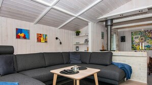 A modern living room with a grey sectional sofa, a wooden coffee table, and a black rug. There are two paintings on the wall, a bookshelf, and a fireplace with a decorative mirror. - 6 Person Holiday Home in Ebeltoft-by Traum (Ebeltoft)