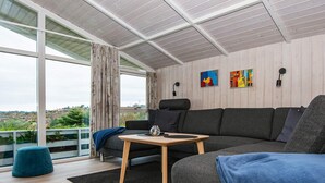 A modern living room with a grey sofa, a wooden coffee table, and a view of the outdoors through large windows. - 6 Person Holiday Home in Ebeltoft-by Traum (Ebeltoft)
