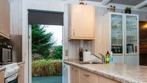 A modern kitchen with a built-in oven, microwave, and sink. There is a glass cabinet with wine glasses and a small plant on top. - 6 Person Holiday Home in Ebeltoft-by Traum (Ebeltoft)