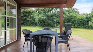 Eine überdachte Terrasse mit einem Holztisch und Stühlen, einem kleinen runden Tisch und einem grünen Sessel.