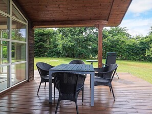 Eine überdachte Terrasse mit einem Holztisch und Stühlen, einem kleinen runden Tisch und einem grünen Sessel.