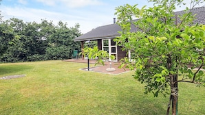 Ein Haus mit überdachter Terrasse, Rasen und Baum im Vordergrund.