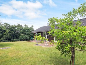 Ein Haus mit überdachter Terrasse, Rasen und Baum im Vordergrund.