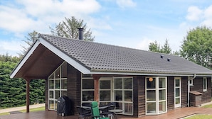 Ein modernes Haus mit einer großen Terrasse, einer überdachten Veranda und einem Schornstein.