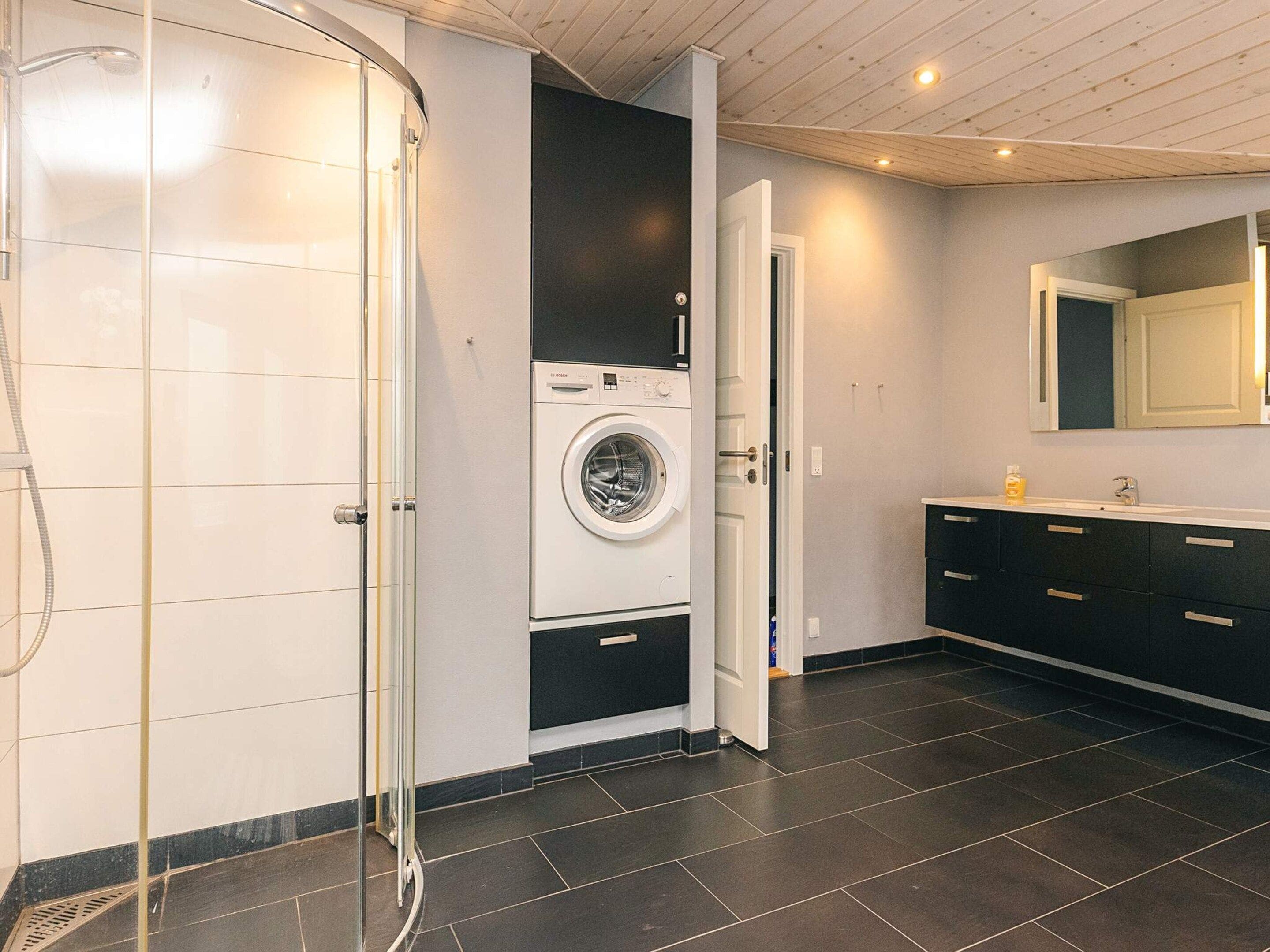 A modern bathroom with a glass shower enclosure, a built-in washing machine, and a vanity with a mirror.