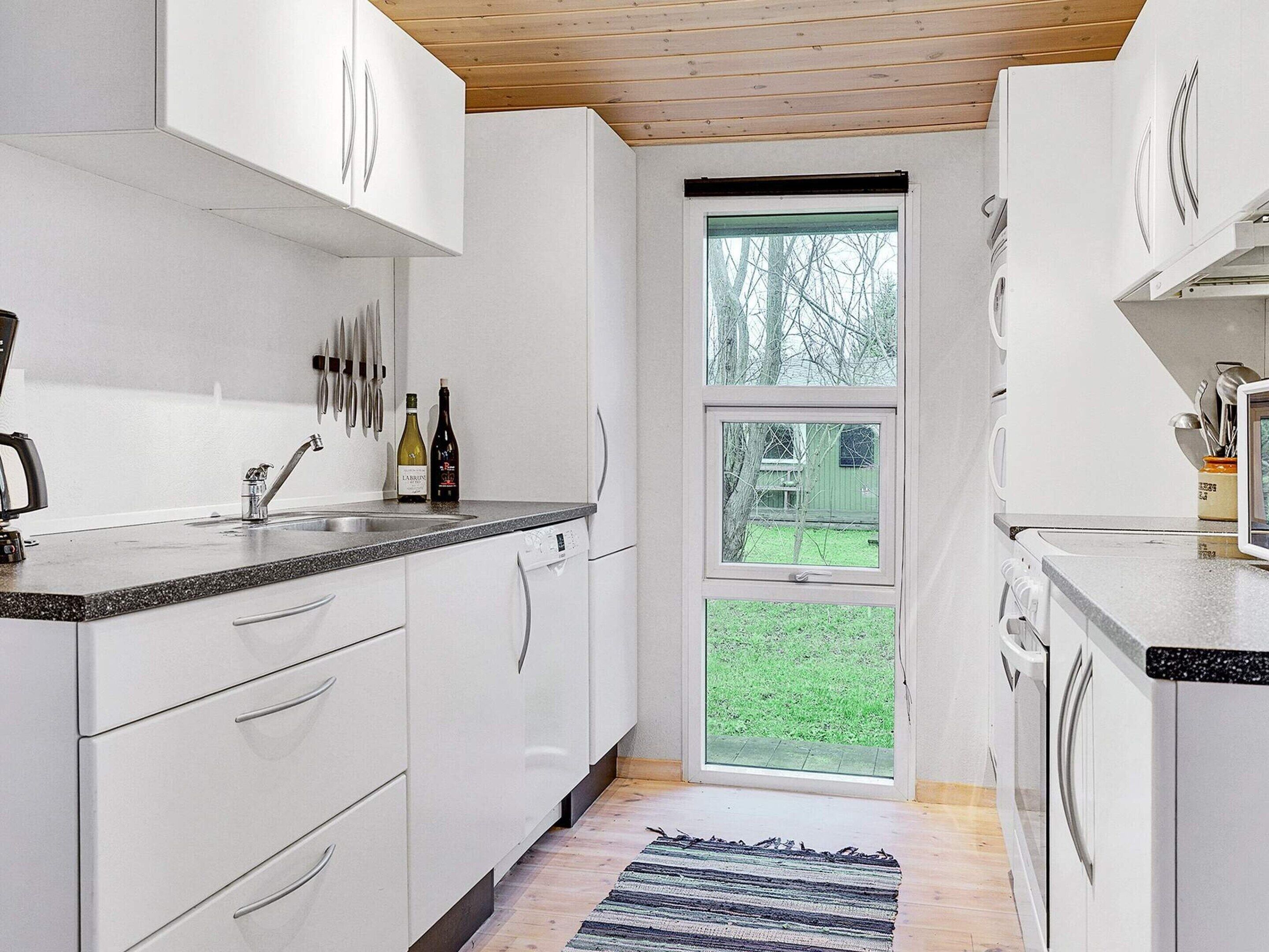 A modern kitchen with white cabinets, a granite countertop, and a window with a view of a green lawn.