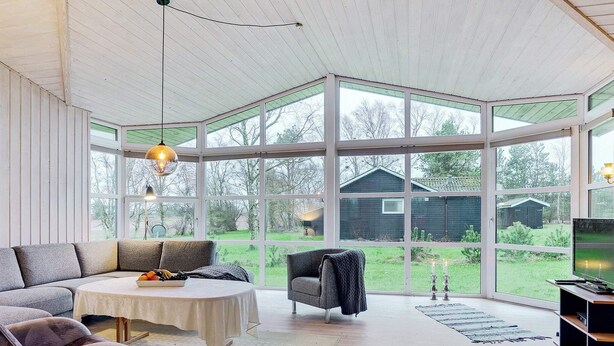 A spacious room with a large window, a sofa, a table, and a chair. - 4 Star Holiday Home in Saeby (Sæby)