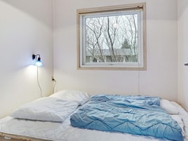 Un dormitorio con una cama individual, una ventana que da a árboles desnudos y una lámpara de pared.