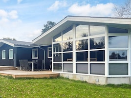 Una casa moderna con una amplia extensión de vidrio, una terraza con mobiliario exterior y un césped bien cuidado.