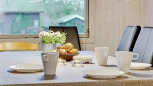 A dining table set with plates, cups, and a bowl of food, with a window and a chair in the background. - 4 Star Holiday Home in Saeby (Sæby)