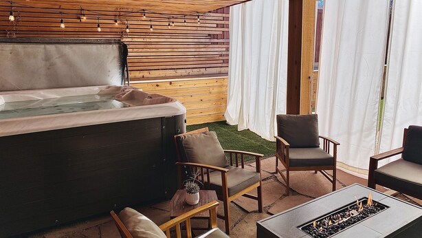 A hot tub with wooden slats, outdoor seating, and string lights.