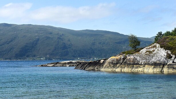 A coastal landscape with a rocky outcrop and a clear view of the sea and distant mountains. - 6 Person Holiday Home in Fiska (Vanylven)