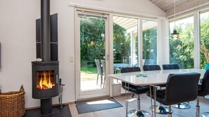 A modern room with a wood-burning stove, a dining table with chairs, and large windows offering a view of the outdoors. - 8 Person Holiday Home in Ebeltoft (Ebeltoft)