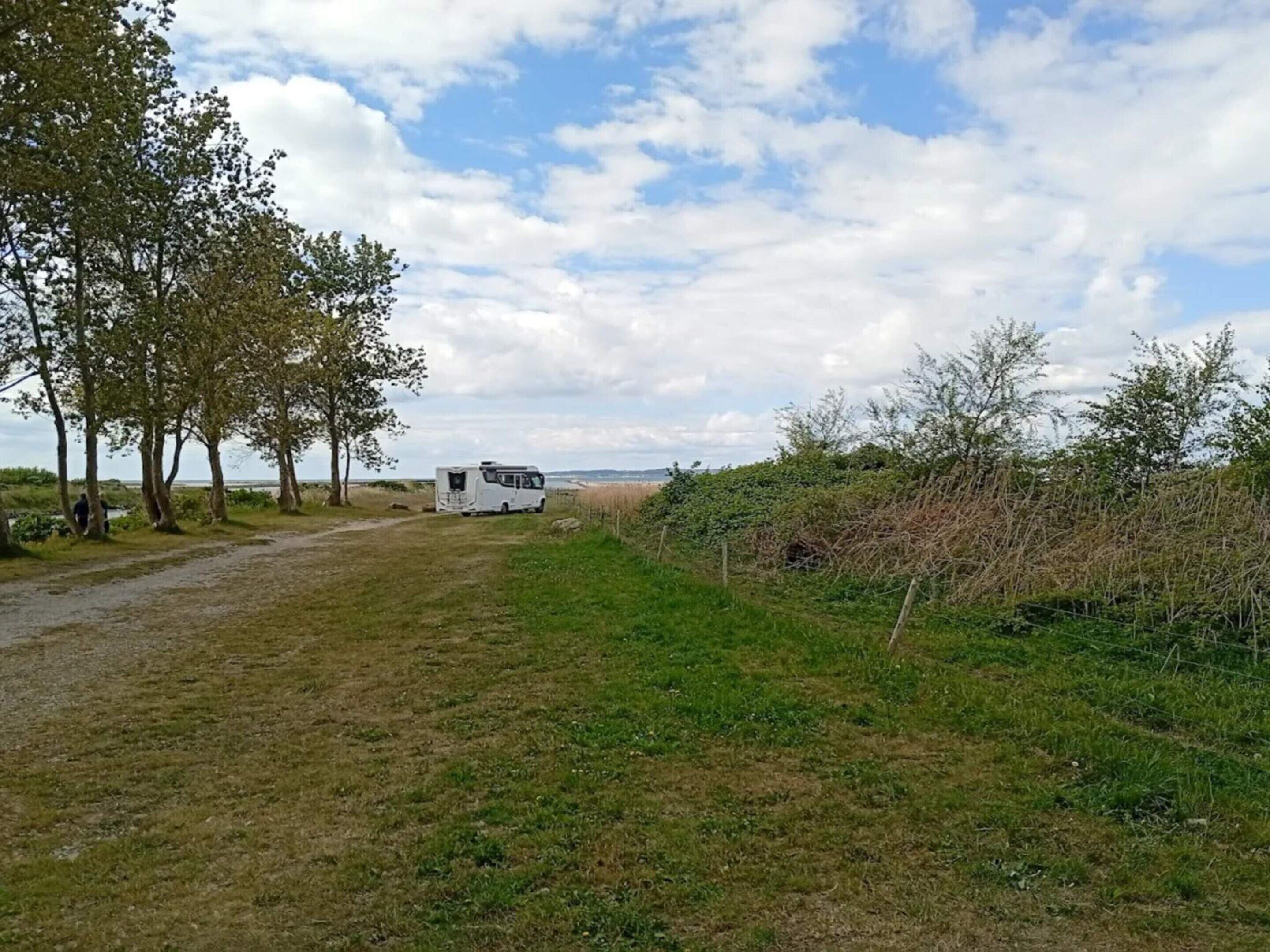 A campsite with a caravan, trees, and a grassy field.