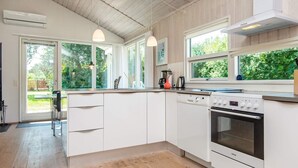 A modern kitchen with white cabinets, a built-in oven, and a dishwasher. There are large windows providing natural light and views of greenery outside. - 8 Person Holiday Home in Ebeltoft (Ebeltoft)